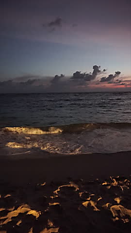 Ocean waves reaching the sandy beach during a calm sunset with clouds on the horizon.