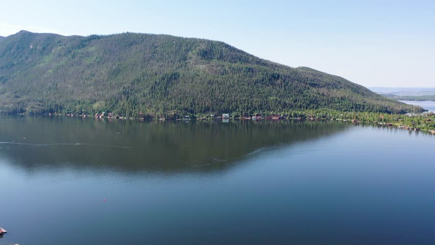 Drone view across Grand Lake Colorado showing the lakefront village, mountain backdrop, wooded neighborhoods, and shoreline development in a picturesque summer landscape