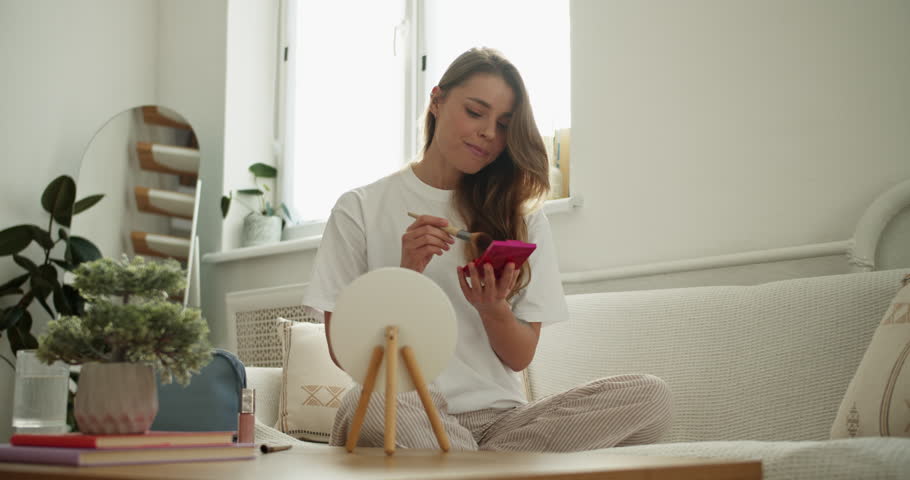 Smiling girl enjoying her morning routine, applying face powder with a brush for a natural look