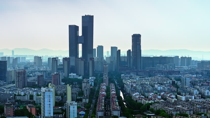 Modern skyline of Nanjing city in China, featuring towering interconnected skyscrapers and dense residential districts under a clear sky with mountain ranges in the distance.