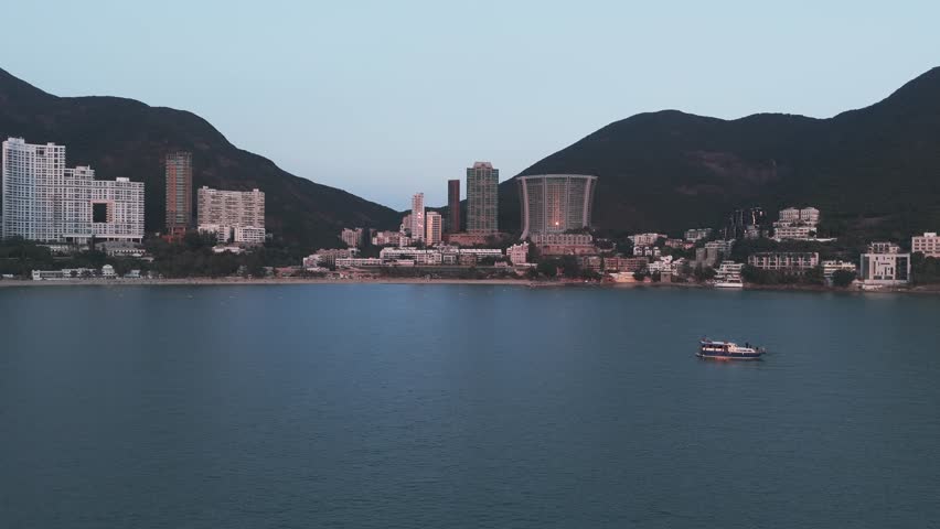 Drone aerial of Repulse Bay, Hong Kong, showing sandy beach, turquoise waters, and high-rise buildings along the coast with panoramic urban skyline.