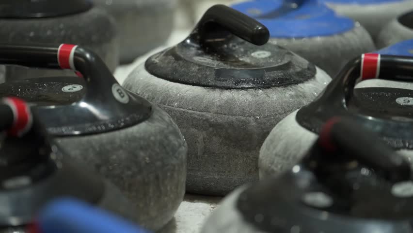 Close view of curling stones arranged on ice rink indoors. Granite stones with colored handles prepared for winter sport training, competition and professional tournament play.