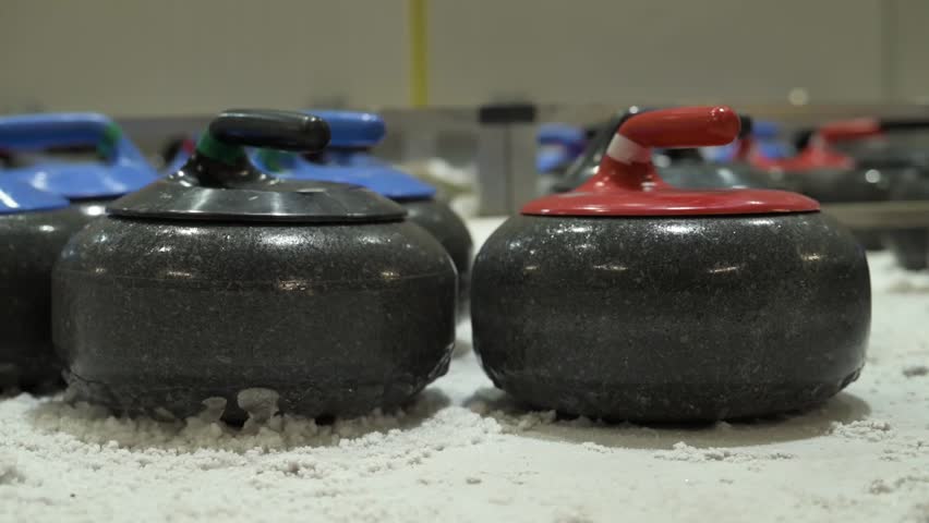 Close view of curling stones arranged on ice rink indoors. Granite stones with colored handles prepared for winter sport training, competition and professional tournament play.