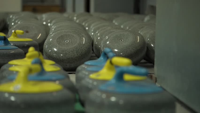 Close view of curling stones arranged on ice rink indoors. Granite stones with colored handles prepared for winter sport training, competition and professional tournament play.