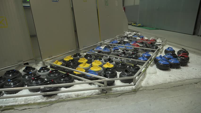 Close view of curling stones arranged on ice rink indoors. Granite stones with colored handles prepared for winter sport training, competition and professional tournament play.