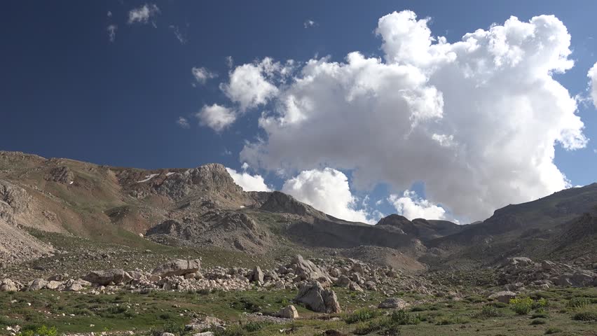 Time lapse of partly cloudy sunny skies above treeless stony hills in the Andes mountains. Sunlit cumulus drift over barren rocky highlands along a rugged Andean cordillera landscape.