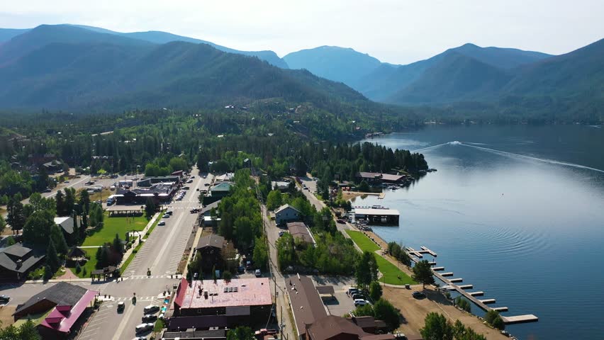 Aerial view above Grand Lake Colorado revealing the mountain town along the water, with quiet streets, lakeside buildings, evergreen trees, and sweeping alpine peaks in the distance
