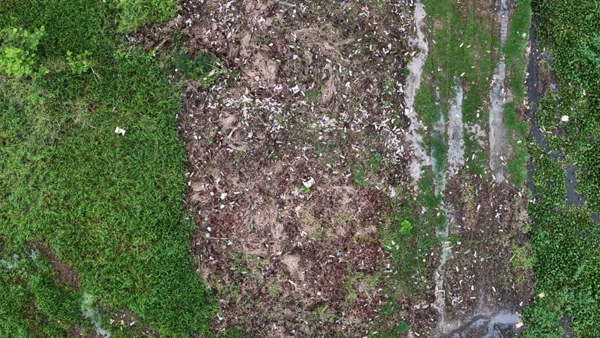 Drone shot aerial rubbish view of rural field with scattered litter, dry grass, and muddy tracks.