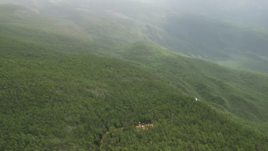 Aerial view revealing a dramatic natural basin inside the mountains with dense green forest and expansive wilderness scenery.