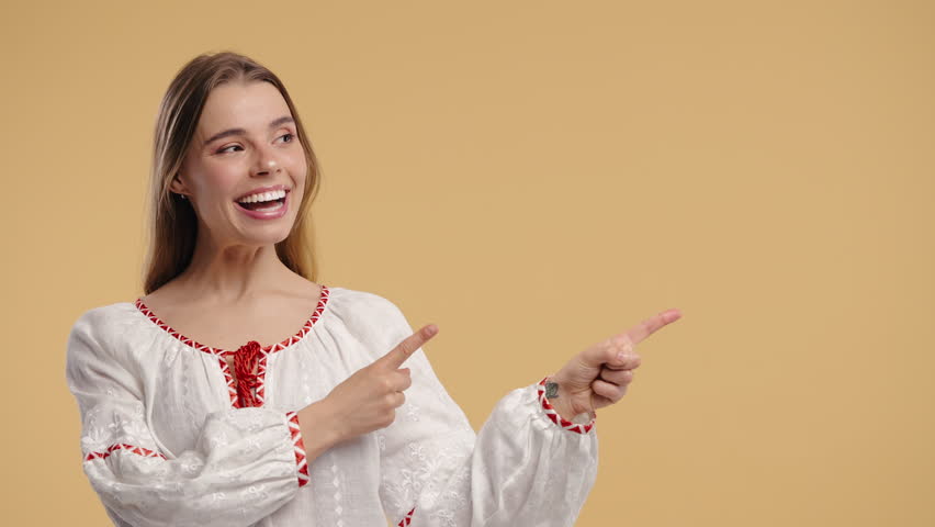 Happy smiling woman presenting and showing something isolated on beige background. Portrait of pretty lady, pointing with arms on copy space.
