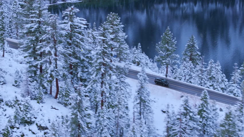 Drone aerial of snow covered Highway 89 winding beside Lake Tahoe with evergreen forest and calm winter water. Scenic alpine winter setting. Emerald Bay, Lake Tahoe, California, USA.