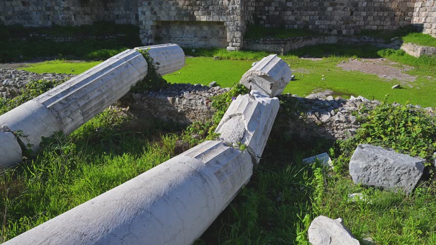 Fallen ancient stone columns lying among archaeological ruins in the western archaeological zone of Kos, Greece as the camera pans to the right