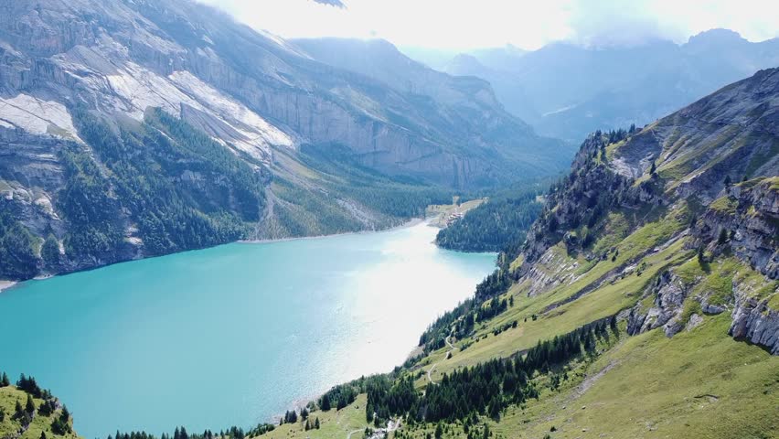 Aerial view of turquoise alpine lake surrounded by mountains and forest