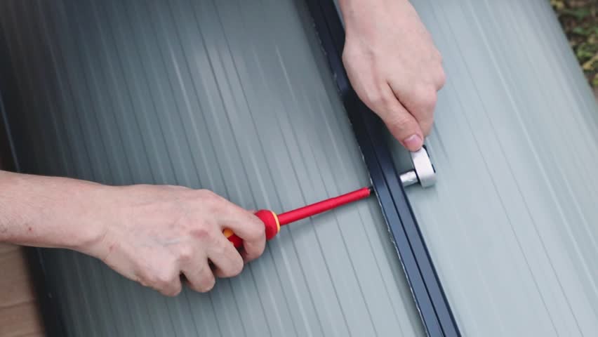 An unrecognizable handyman installs side mounts on a metal barn door using screwdrivers.