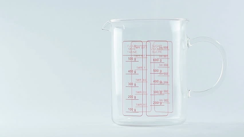 Sugar being measured and poured into translucent glass, white isolated background