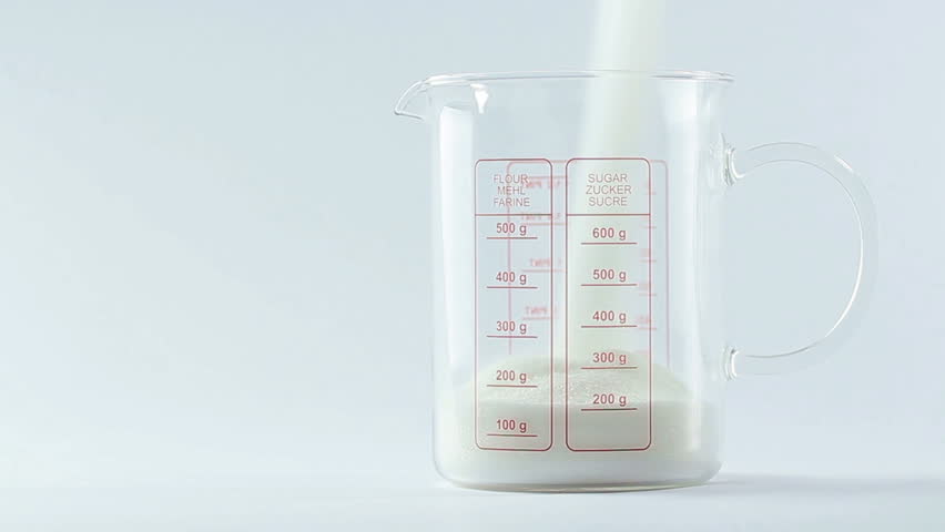 Sugar being measured and poured into translucent glass, white isolated