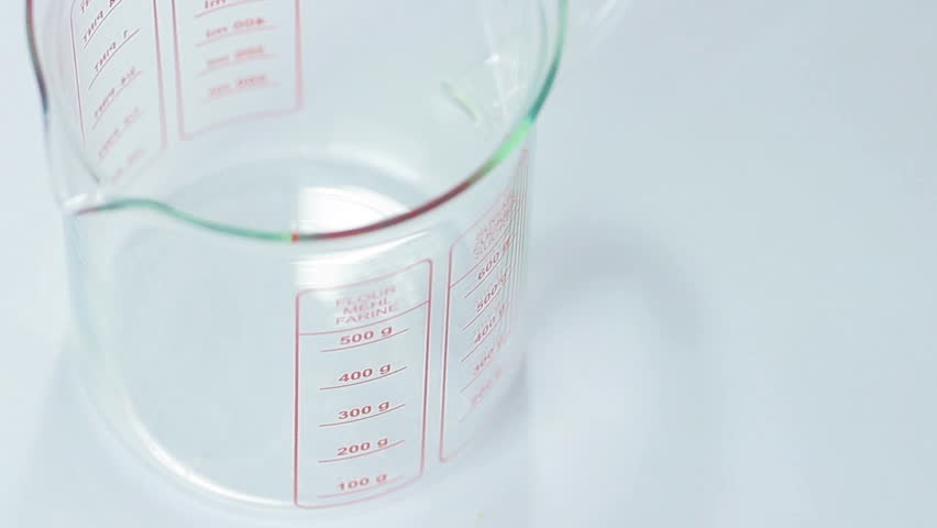 Sugar being measured and poured into translucent glass, white isolated background