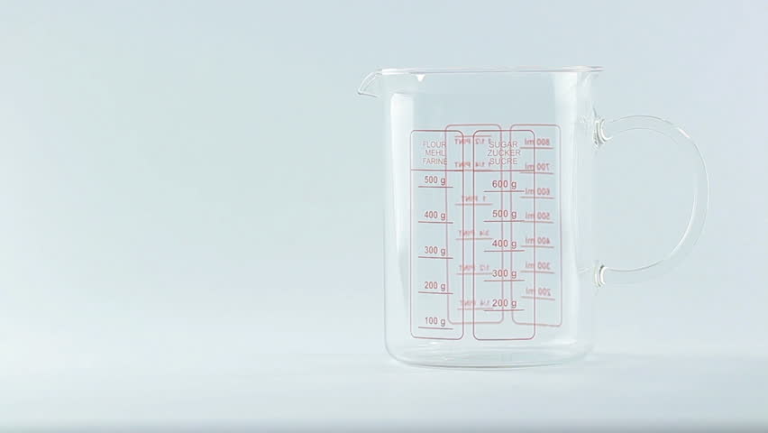 Flour being measured and poured into translucent glass, white isolated