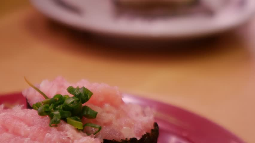 Negitoro minced fatty tuna gunkan maki sushi topped with green onion on red plate, Japanese restaurant