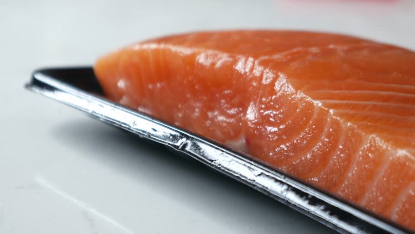 Fresh raw Atlantic salmon fillet portion on black plastic supermarket tray on white marble kitchen countertop, ready to cook