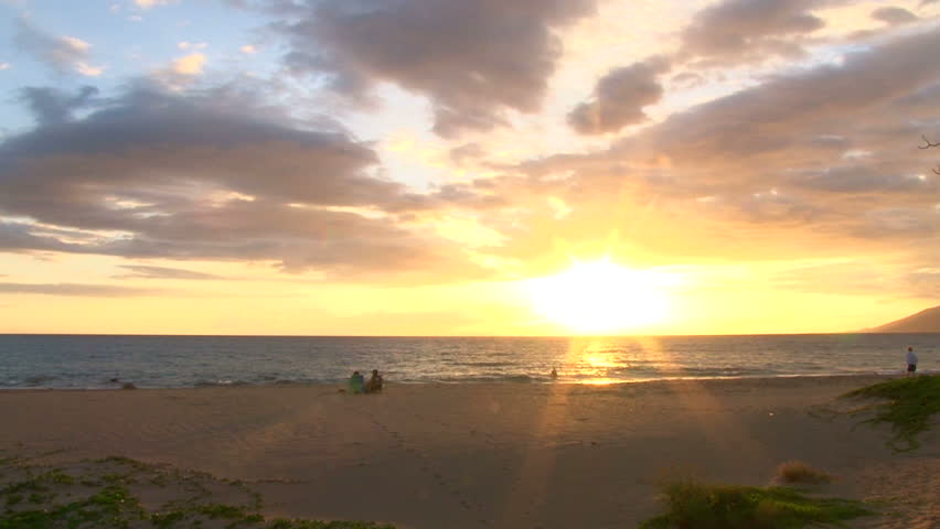 People watch sun go down in Hawaii on sandy beach, real time.