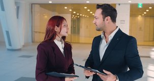Two professional colleagues holding folders discuss corporate strategy while standing in bright modern office hall lobby during morning meeting - Powered by Shutterstock - Get 15% off with code: PIKWIZARD15