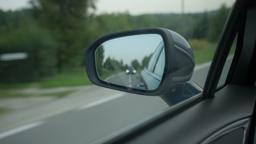 Close up of car side mirror with road and vehicle reflected while driving on rural road. Concept of travel, transport, traffic and driving