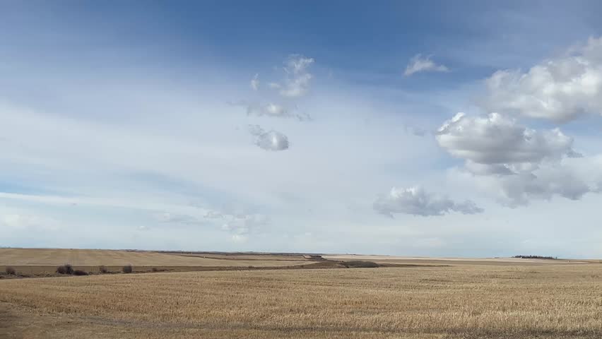 Open prairie farmland under blue sky with scattered clouds in Alberta Canada