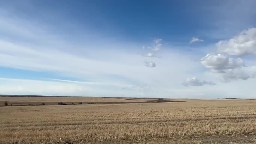 Open prairie farmland under blue sky with scattered clouds in Alberta Canada