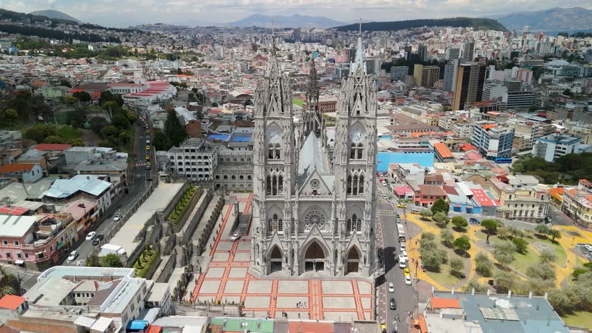 Aerial parallax orbits full Basílica del Voto Nacional neo-gothic twin spires flying buttresses forecourt plaza against Quito cityscape