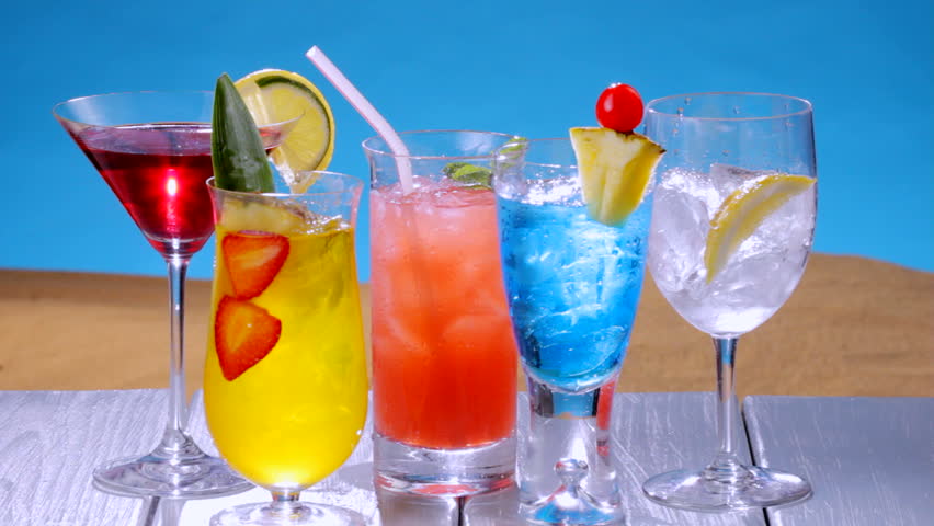 Several colorful summer drinks on table as iced tea is poured into a glass, shot