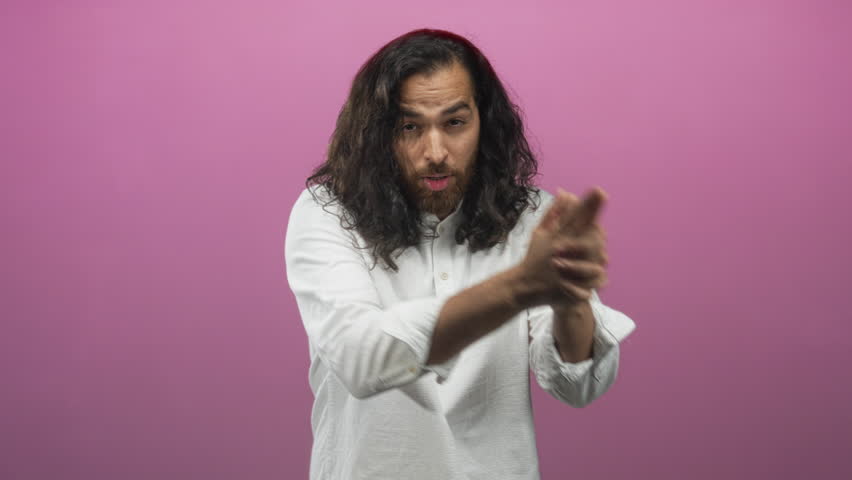 Man forming finger gun with both hands and direct gaze in pink studio closeup, wearing white shirt; focus determination.