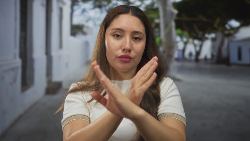 Woman stands with hands on hips on sunlit narrow city street lined with white walls; confidence independence.