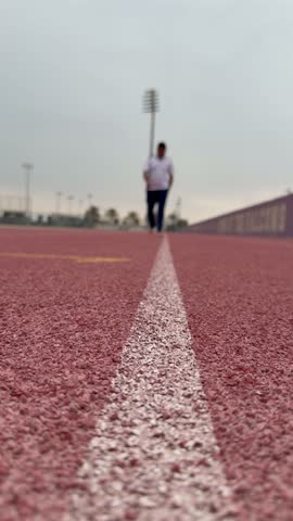 A man walks along the NYUAD rubber track, following a straight, simple line that feels symbolic and quietly purposeful.