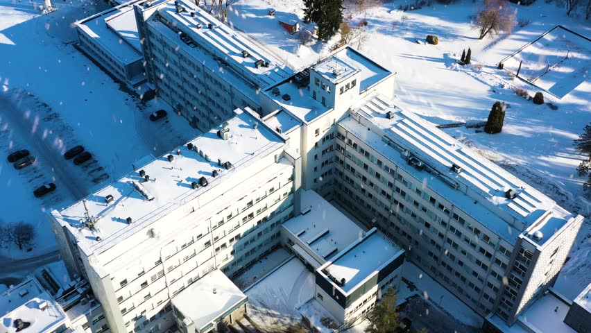 Hospital building complex covered in snow, specializing in healthcare and medicine in aerial top down view on a sunny winter day