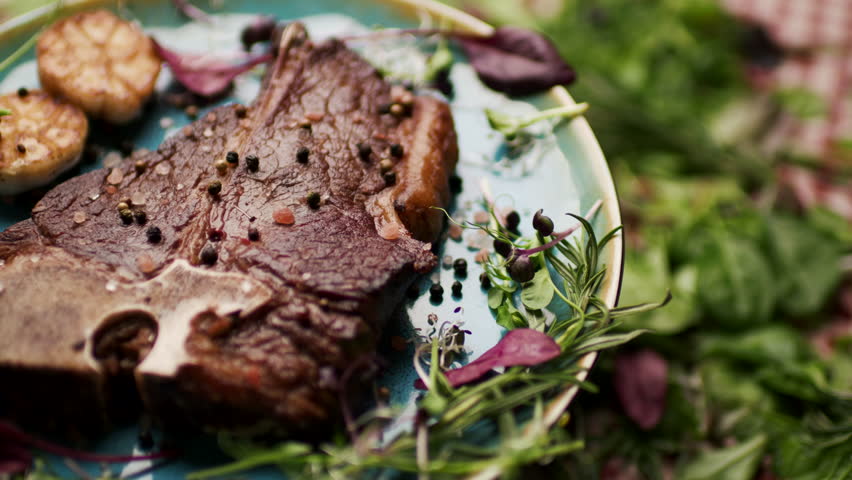 Grilled T-Bone Steak Rotating on Table with Fresh Greenery