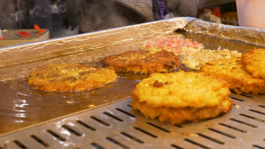 Slow motion close-up of crispy Bindaetteok seafood pancake street food cooking on hot grill stove top with oil at Gwangjang night markets in Seoul city South Korea traditional cuisine culinary snack