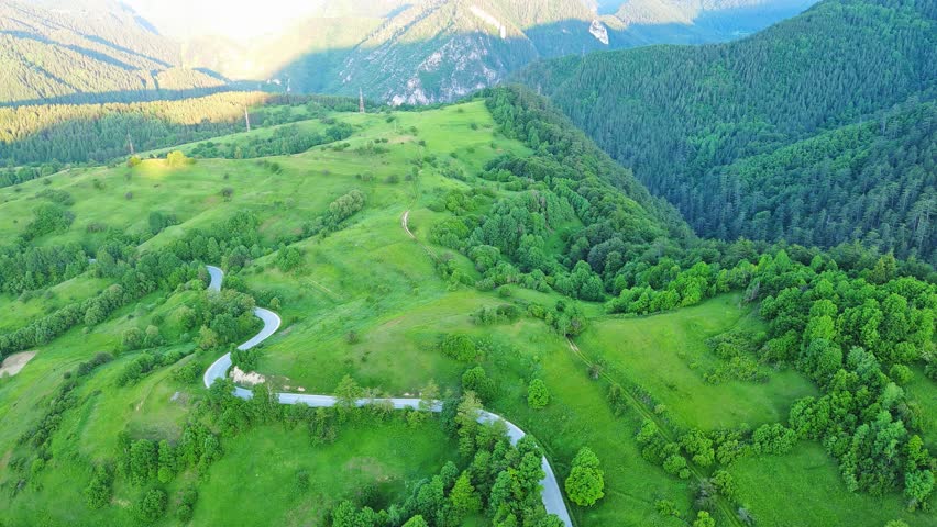 A road passes hills covered with spruce forests and meadows against a cloudy sky