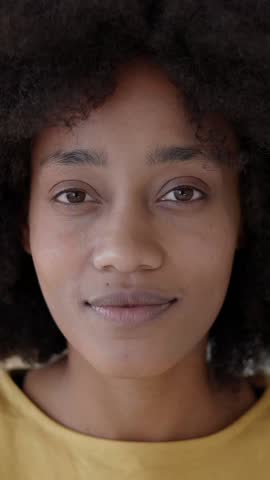 Vertical headshot portrait of a confident young black woman with a curly afro hairstyle looking directly at the camera with a gentle and warm smile, showcasing her natural beauty and positive attitude