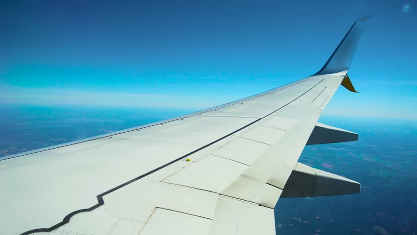 Aircraft flying above patchy forest and farmland. Passenger jet cruising over green and brown rural terrain. Commercial airplane gliding across mixed landscape of fields and woods