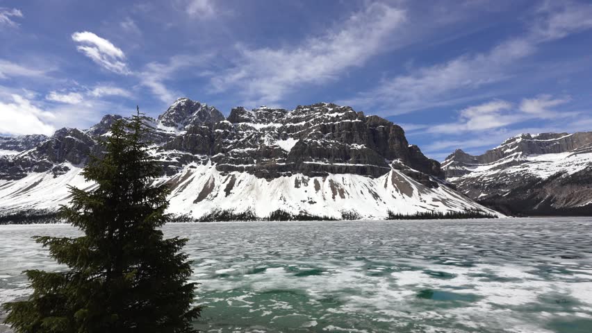 Frozen Bow Lake showing ice melting with snow capped mountains and blue sky in Banff National Park