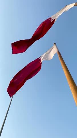 Qatar national flags waving on tall flagpoles against a clear blue sky in Doha. Time Lapse 