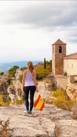 happy female tourist in Spain holding spanish flag on top of mountain