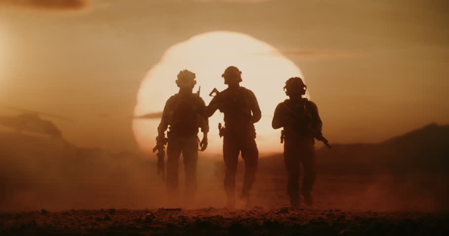 Three Armed Soldiers in Silhouette Walk Across Desert at Sunset While a Helicopter Flying in Background. Patrol During a Mission, Active Warfare, Conflict, Military Operation. Slow Motion Cinematic