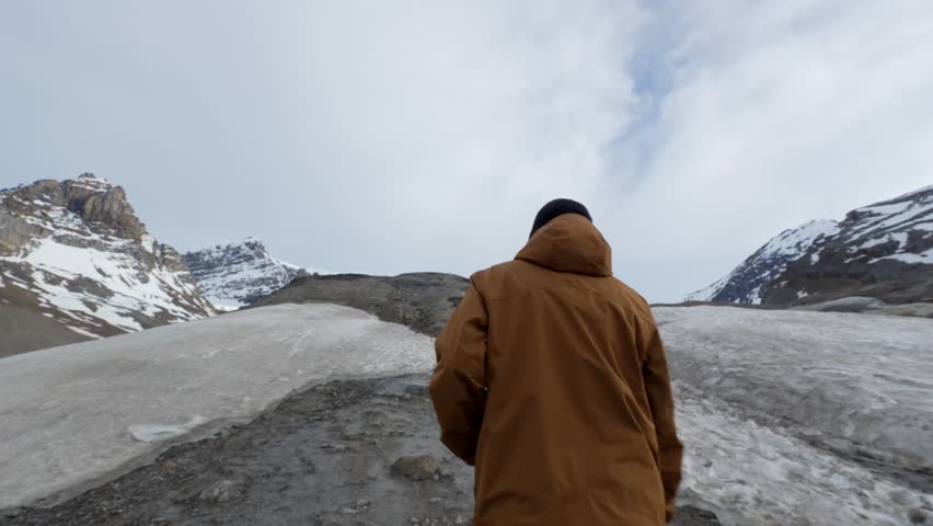 Man walking on road towards Athabasca Glacier under cloudy sky in Jasper National Park