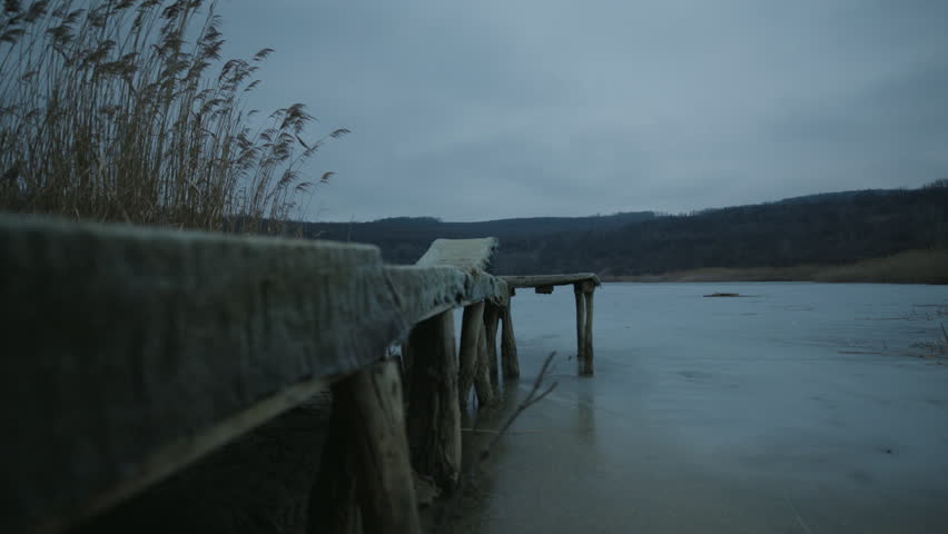 Frozen lake surface with circular ice patterns and gas bubbles seen from a wooden pier at dawn. Winter landscape at a dock.