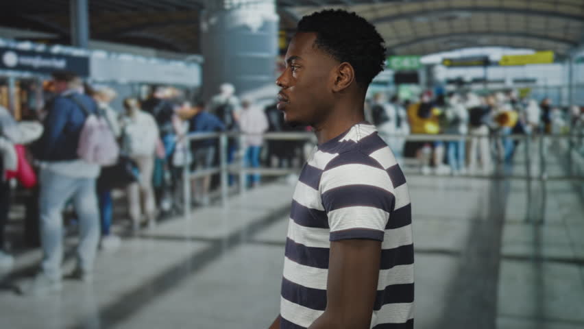 Young african american man looking over shoulder while standing at crowded airport terminal queue; anticipation.