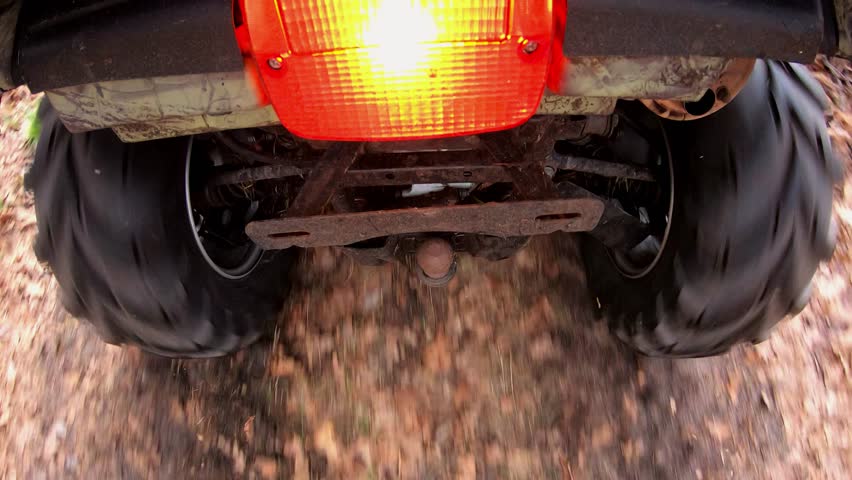 ATV traversing through autumn foliage, showcasing the rugged tires and undercarriage in motion, highlighting the dynamic interaction with the natural terrain and the vibrant environment