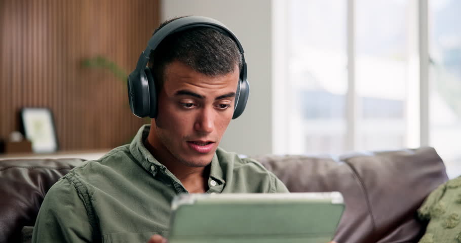 Headphones, tablet and man on sofa with surprise, watch video or movie on internet in living room. Audio, tech and person relax in home with streaming service for show, wow and shocked at film