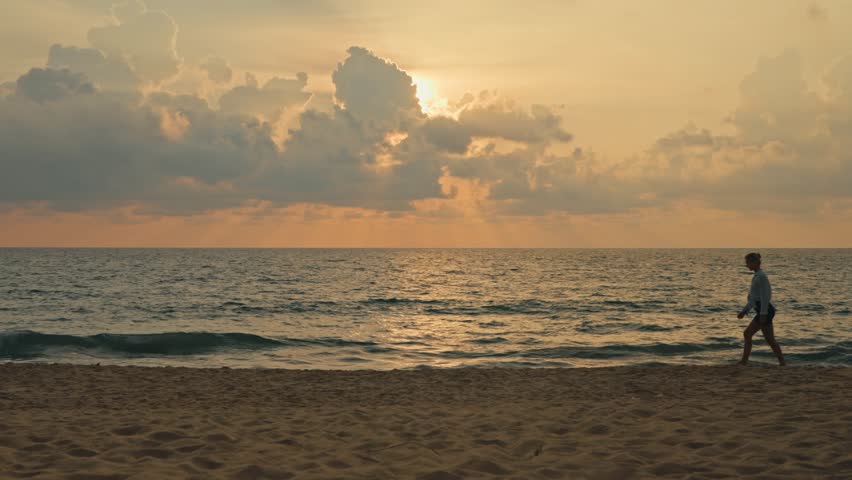 Silhouette of a woman walking along a tropical beach shore during sunset. Gentle waves and warm evening colors create a calm atmosphere as she enjoys a peaceful beach walk